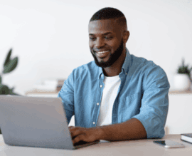 Smiling Black man sitting at a desk using a laptop for an online therapy session