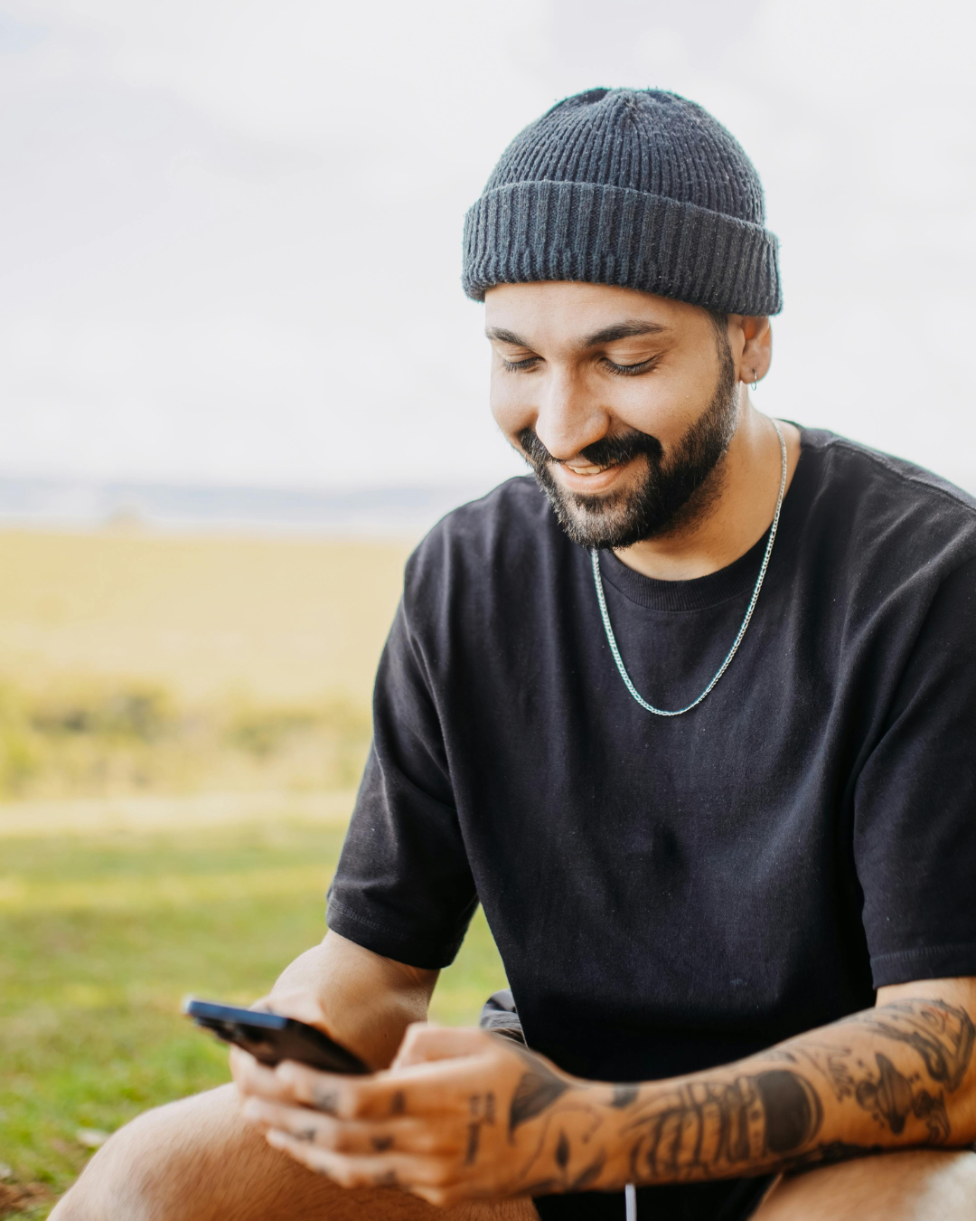 A man sitting outdoors smiling while using his phone for an online therapy session, representing flexible telehealth options offered by Lamplight Counseling Services in Ohio.