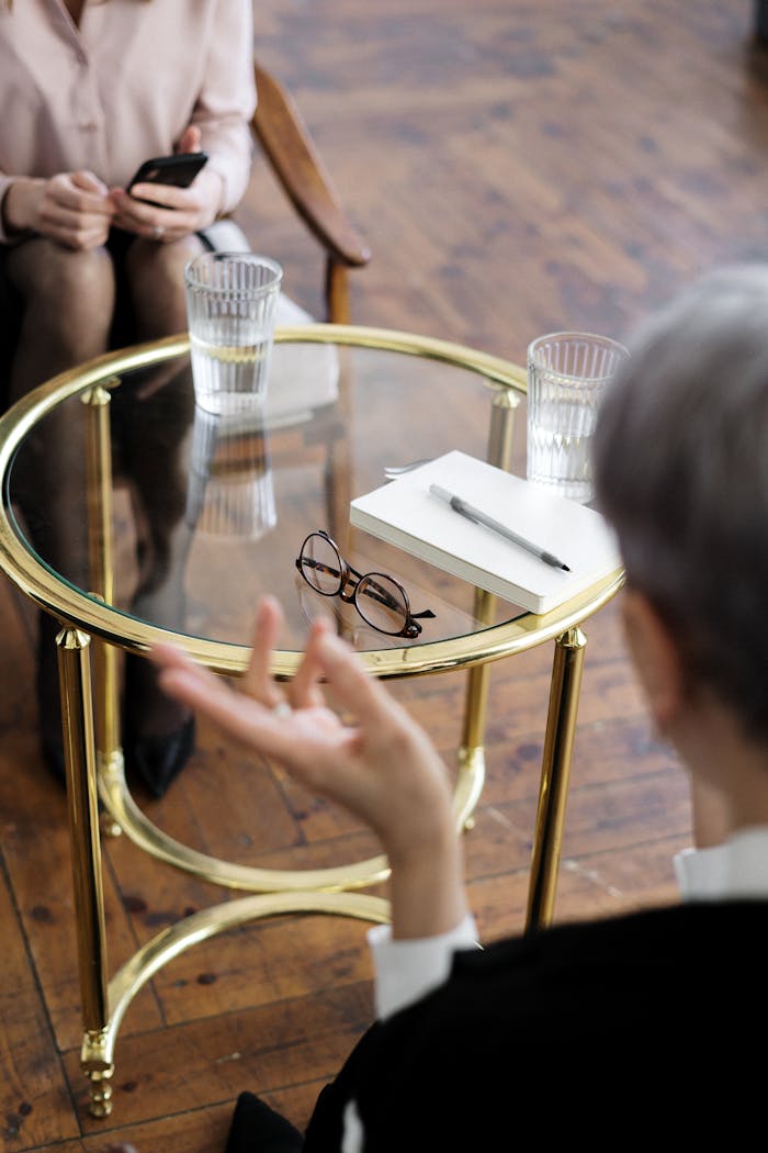 digital Two adults engaged in a therapy session, seated at a glass table with notebooks and water glasses.