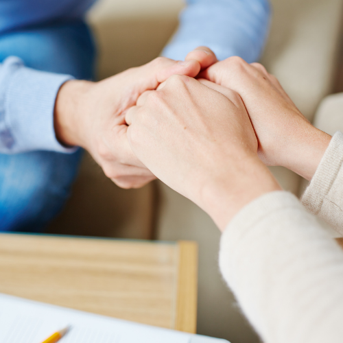 A close-up photo of two people holding hands in a supportive gesture during a counseling session at Lamplight Counseling Services.
