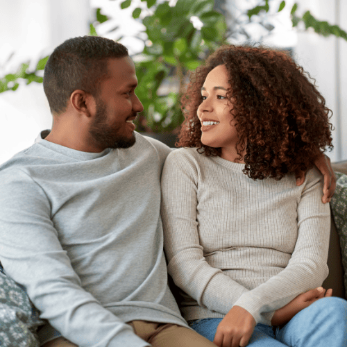 Deepening Connection, Trust, and Relational Wellness A warm, candid photograph of a couple sitting close, the man with his arm around the woman’s shoulders, symbolizing the safety, connection, and restored trust achieved through couples counseling at Lamplight Counseling Services.