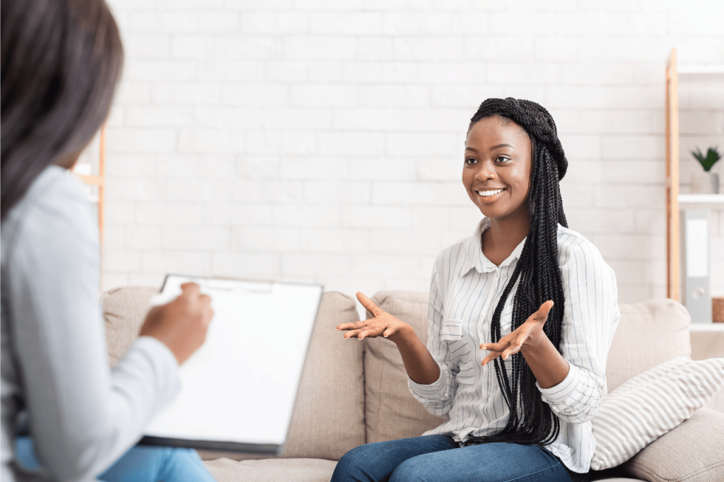 A cartoon illustration of a young woman smiling and talking openly to a therapist, whose back is visible, representing the safe, confidential, and supportive environment for individual therapy at Lamplight Counseling Services.