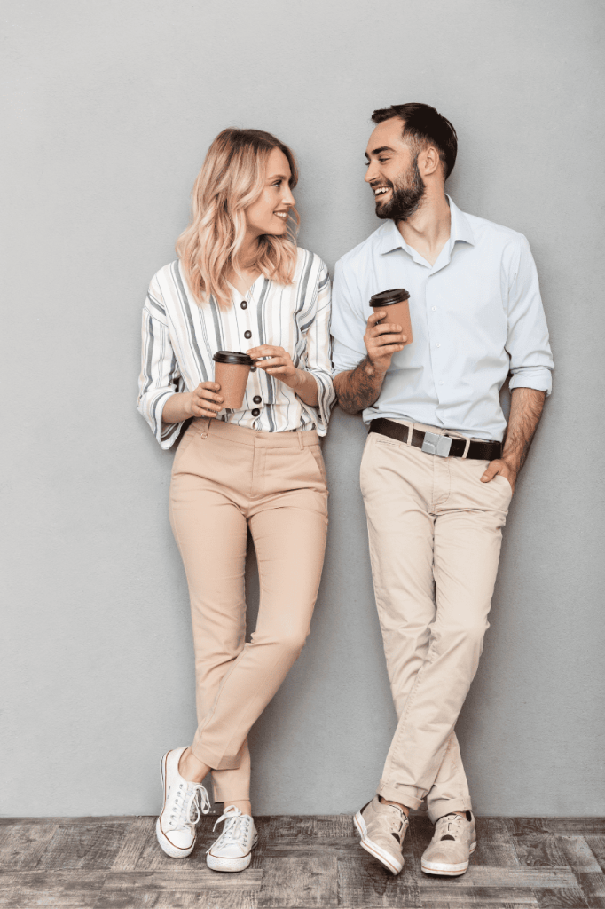 Effective Communication and Couples Counseling – Lamplight Counseling Services man and a woman in khaki clothing standing against a neutral background, holding coffee cups and engaged in a calm conversation.
